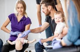 Group of people during the first aid training with instructor showing on manikin how to do artificial respiration for the baby