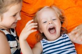 Two little girls lying on orange blanket laughing and having fun