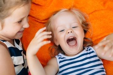 Two little girls lying on orange blanket laughing and having fun