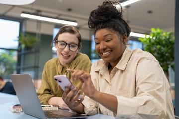 Smiling women at a desk using phone and laptop